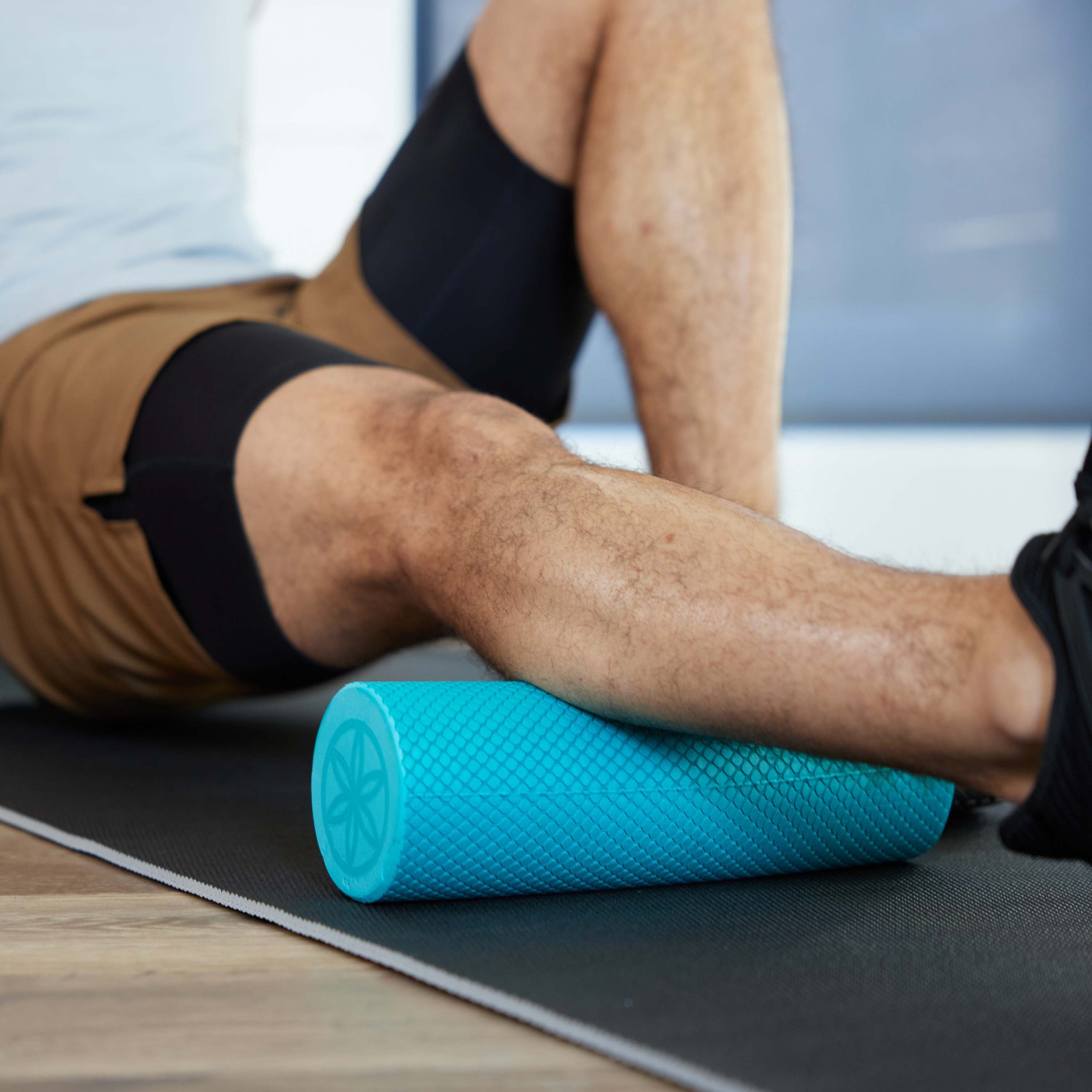 Up close of persons leg on yoga mat with the Restore Compact Foam Roller under the calf